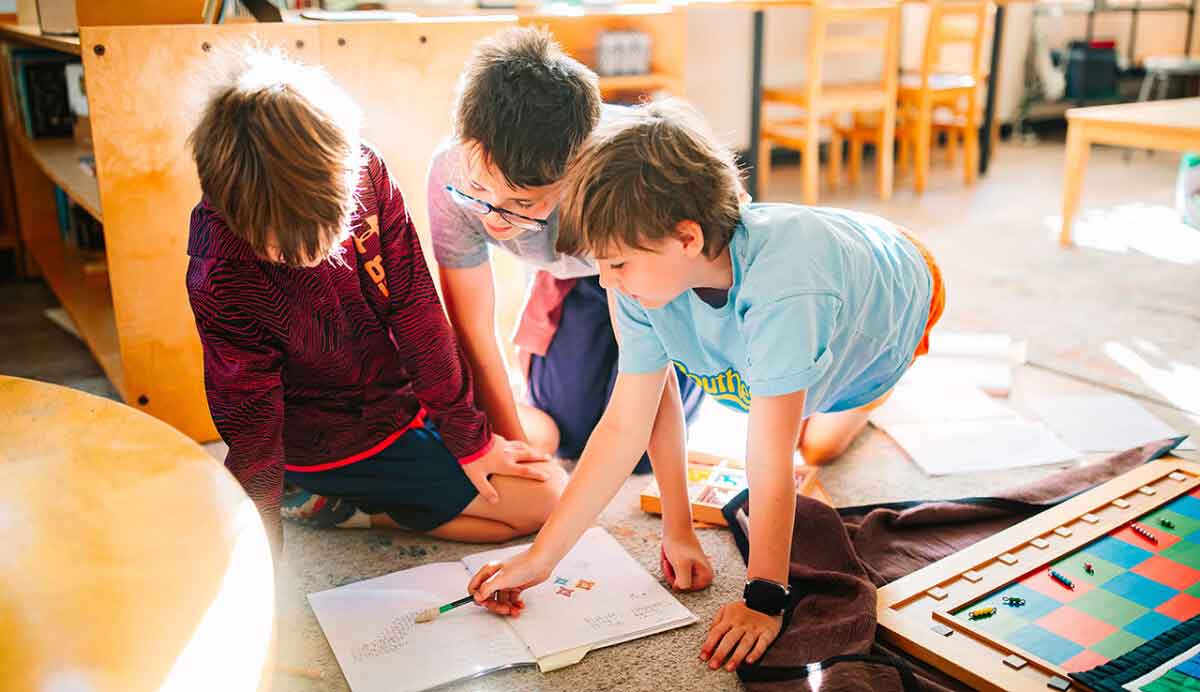 Three boys reviewing book on the floor.