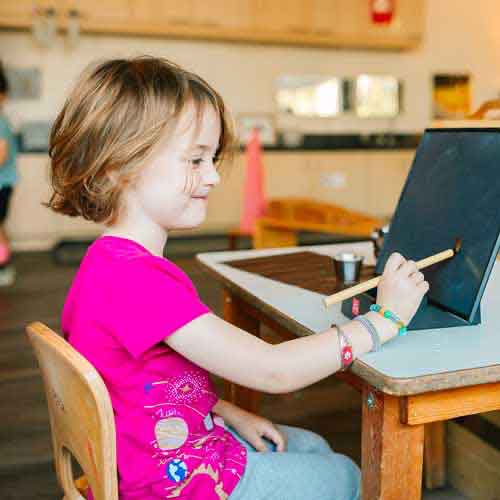 Little girl in pink using paint brush on computer tablet.
