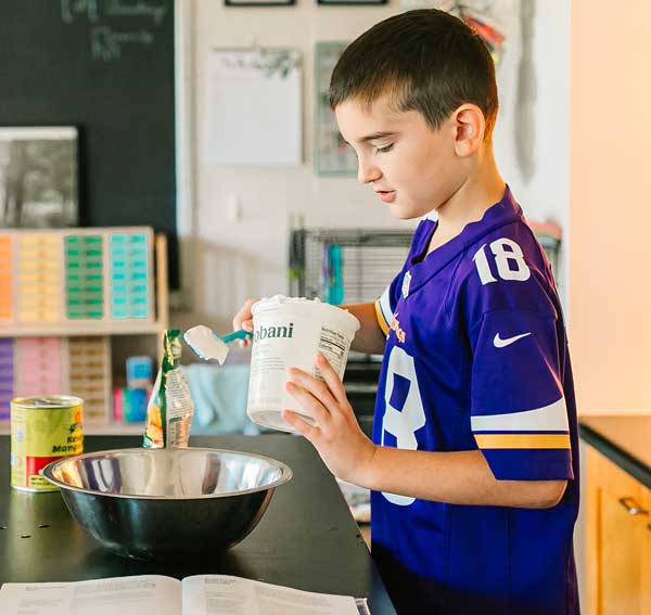 Boy in school kitchen mixing ingredients in a bowl.