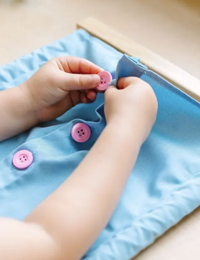 close up of a Montessori students hands working on practical life buttoning